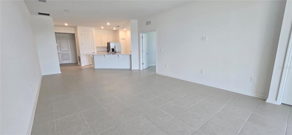 An open-concept living area features light-colored tile flooring and a view of the kitchen — 2451 BLUESTONE ROAD, LAKE HAMILTON, FL