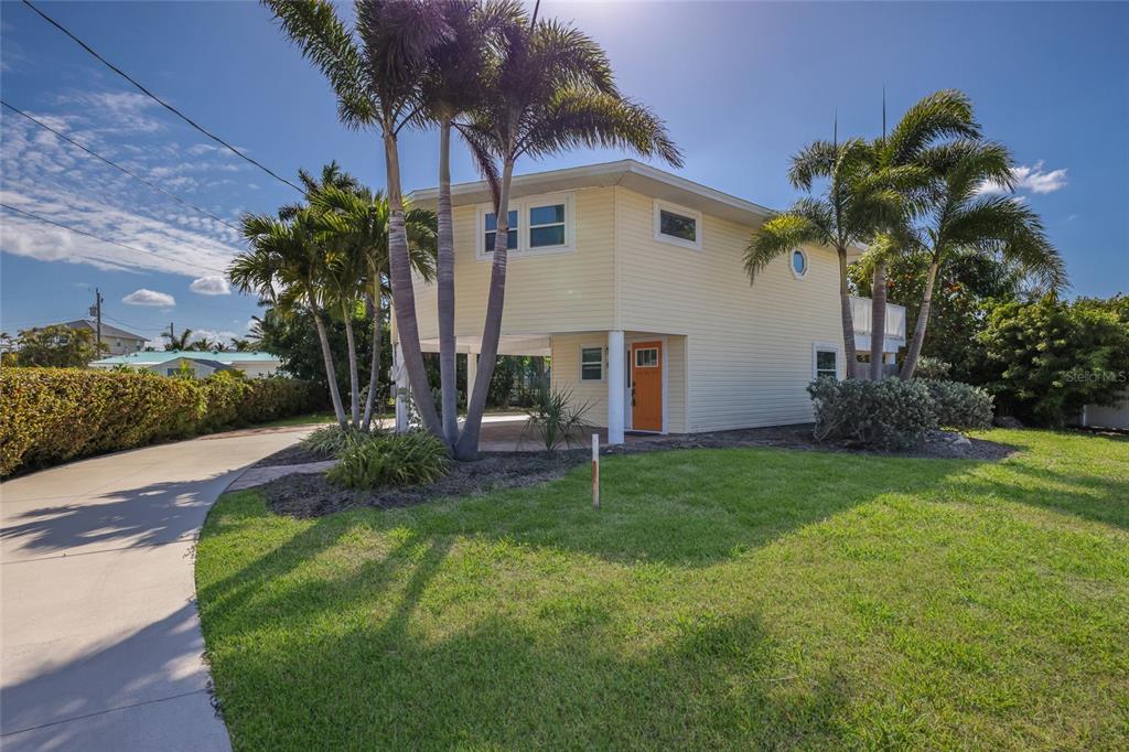 A two-story yellow house with an orange front door stands behind palm trees and grass — 221 85TH STREET, HOLMES BEACH, FL
