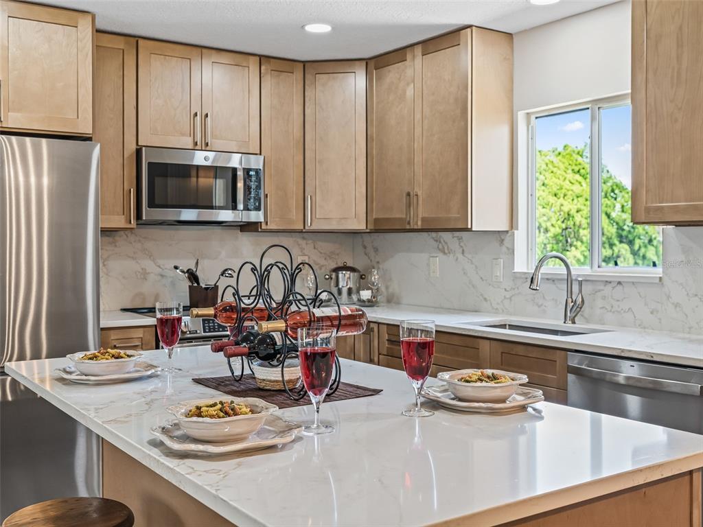 A kitchen features light wood cabinets, white marble-look countertops, and a central island with wine — 17587 SE 106TH AVENUE, SUMMERFIELD, FL