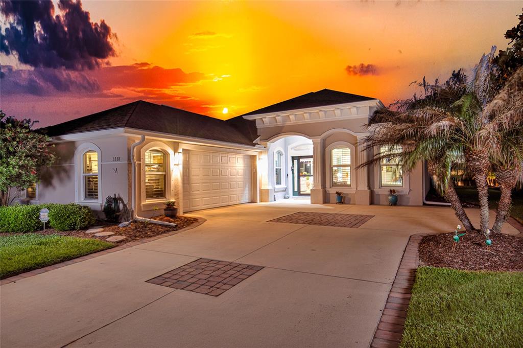 A single-story house with a beige exterior, a two-car garage, and a paved driveway at sunset — 3338 BELLINO BOULEVARD, NEW SMYRNA BEACH, FL