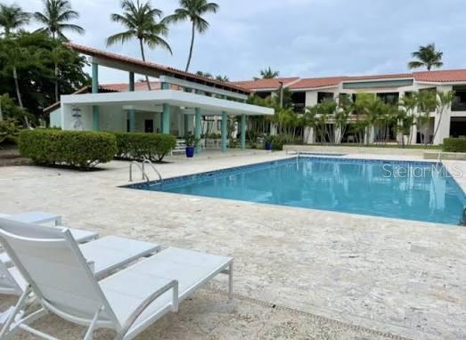 A swimming pool sits on a stone patio in front of a multi-story residential building — Palmas del Mar FAIRLAKES VILLAGE UNIT 655, HUMACAO, PR