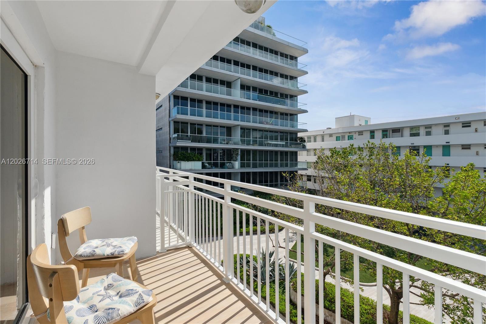 A balcony with two wooden chairs overlooks a courtyard and modern apartment buildings — 325 Ocean Dr # 502, Miami Beach FL 33139, MIAMI BEACH, FL