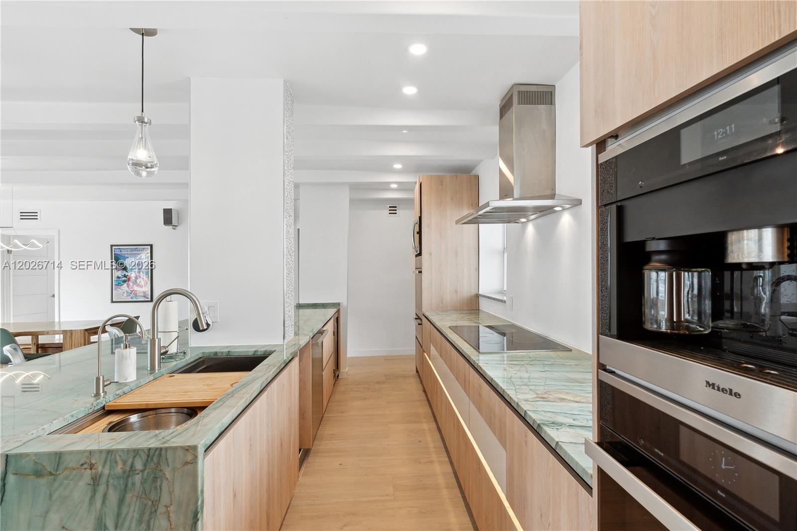 A modern kitchen features light wood cabinetry, green stone countertops, and integrated stainless steel appliances — 325 Ocean Dr # 502, Miami Beach FL 33139, MIAMI BEACH, FL
