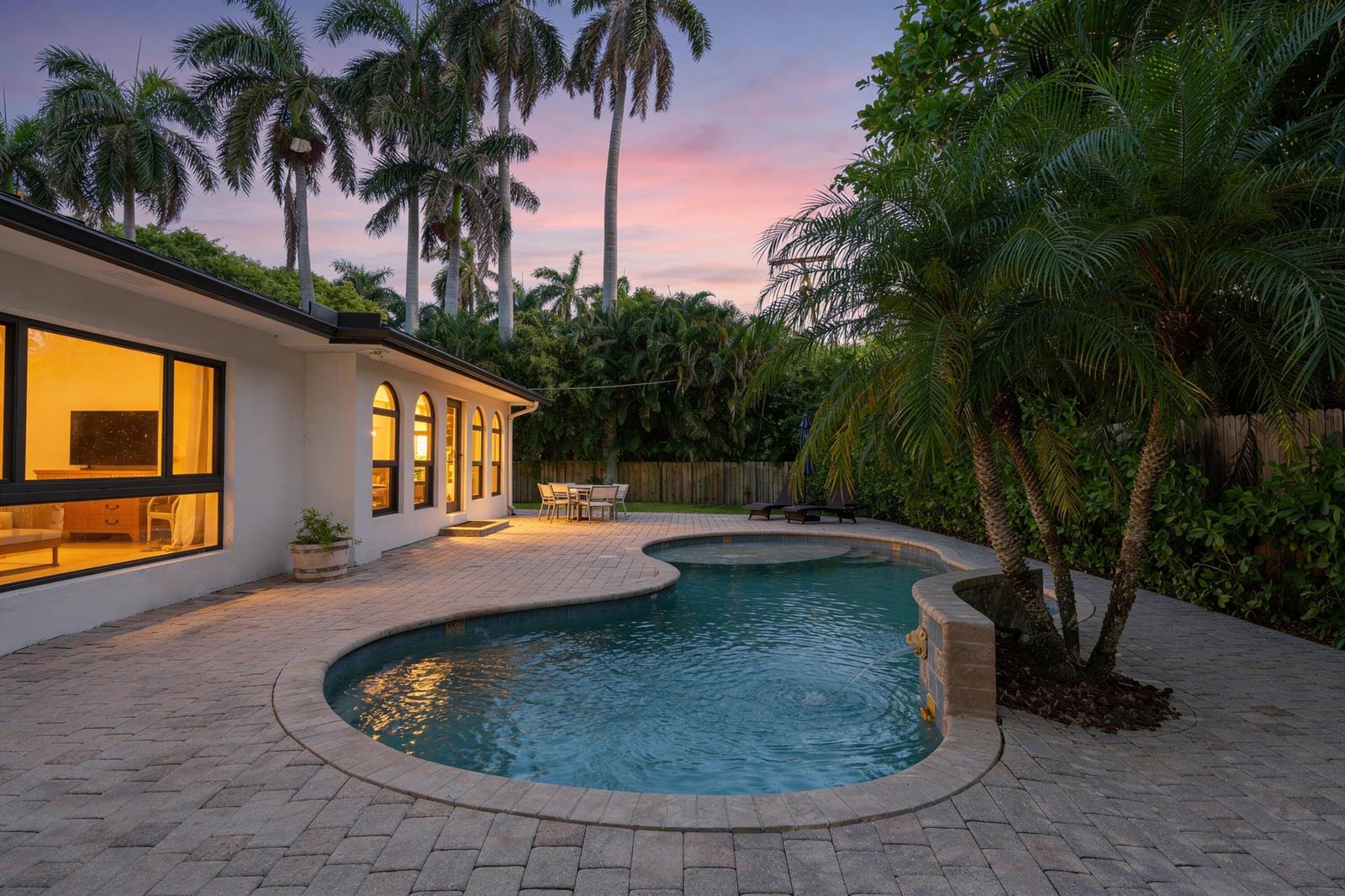 A backyard patio features a curved swimming pool with a fountain next to a house — 35 Anna Street, Ocean Ridge FL 33435, OCEAN RIDGE, FL