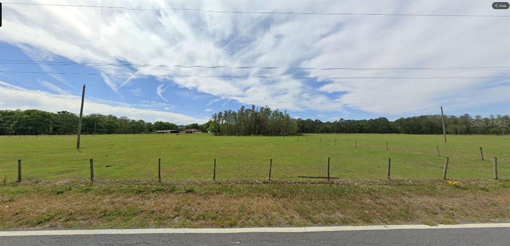 A wide, grassy, fenced-in vacant lot sits alongside a paved road under a cloudy sky — GREEN POND RD, POLK CITY, FL