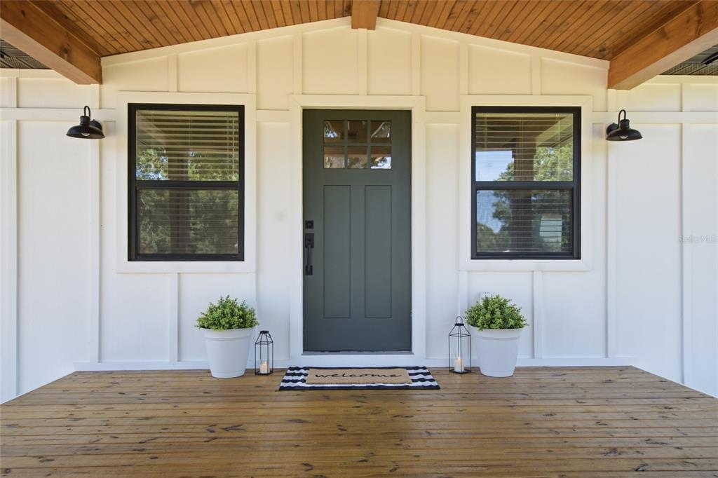 A front porch with a dark green door, white board-and-batten siding, and wood ceiling — 3845 RAMBLER AVENUE, ST CLOUD, FL
