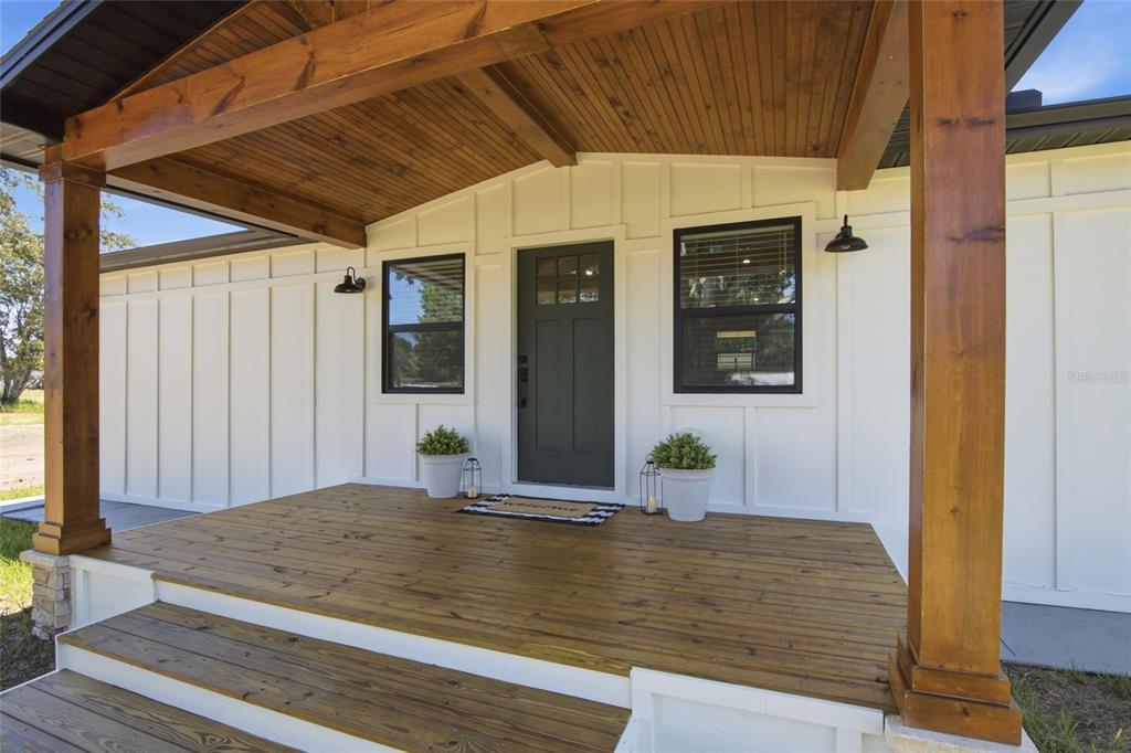 A front porch with wooden decking and ceiling, white board-and-batten siding, and a dark door — 3845 RAMBLER AVENUE, ST CLOUD, FL