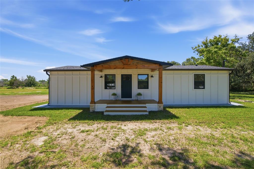 A single-story white house with a wooden front porch sits on a grassy lot — 3845 RAMBLER AVENUE, ST CLOUD, FL