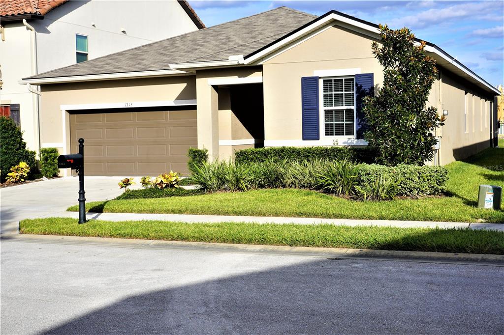 A single-story suburban house features a tan exterior, a brown garage door, and blue shutters — 1315 YORKSHIRE COURT, DAVENPORT, FL