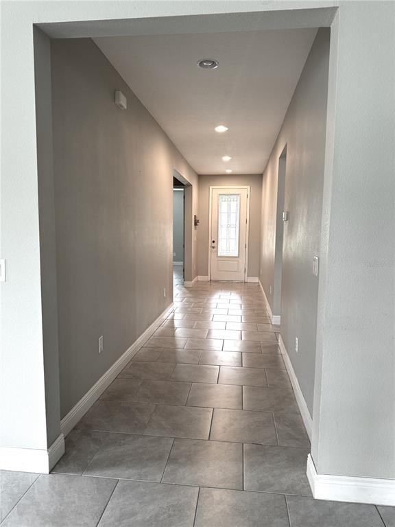 A long hallway with gray walls and light-colored tile flooring leads to an exterior door — 1315 YORKSHIRE COURT, DAVENPORT, FL