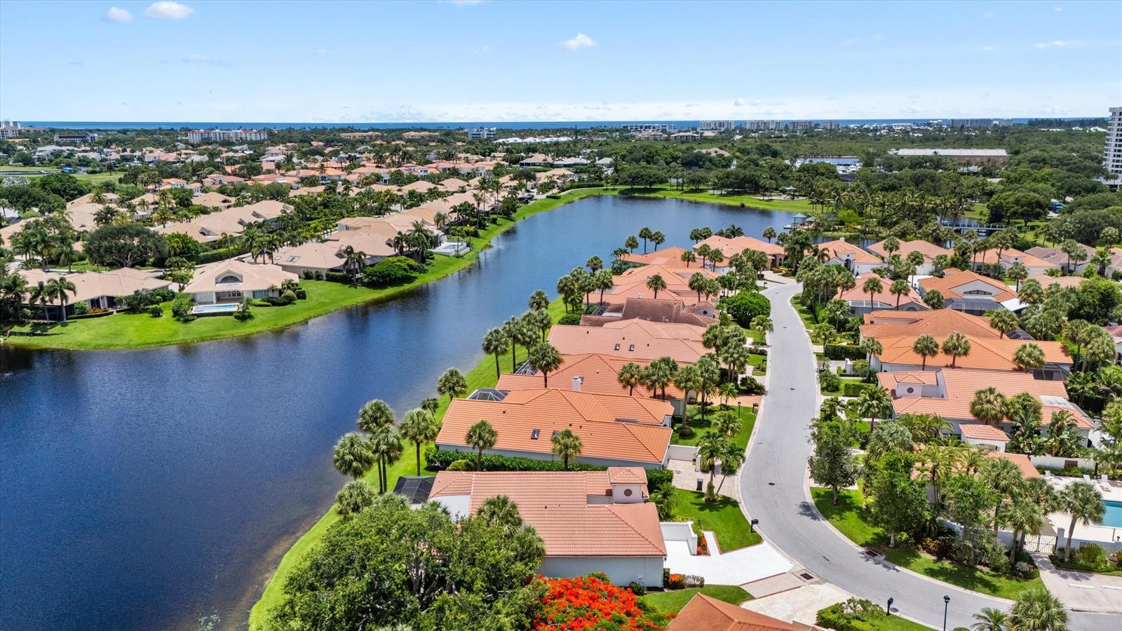 An aerial view shows a residential neighborhood with tile-roofed houses bordering a large lake — 3526 Lantern Bay Drive, Jupiter FL 33477, JUPITER, FL