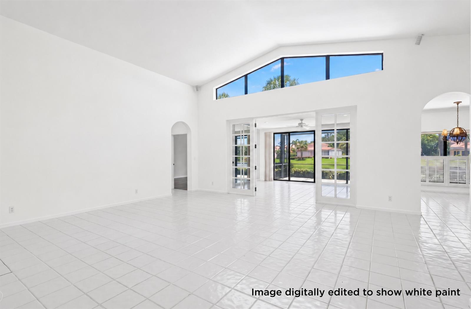 A bright, empty living room with white tile floors, vaulted ceilings, and large glass doors — 3526 Lantern Bay Drive, Jupiter FL 33477, JUPITER, FL