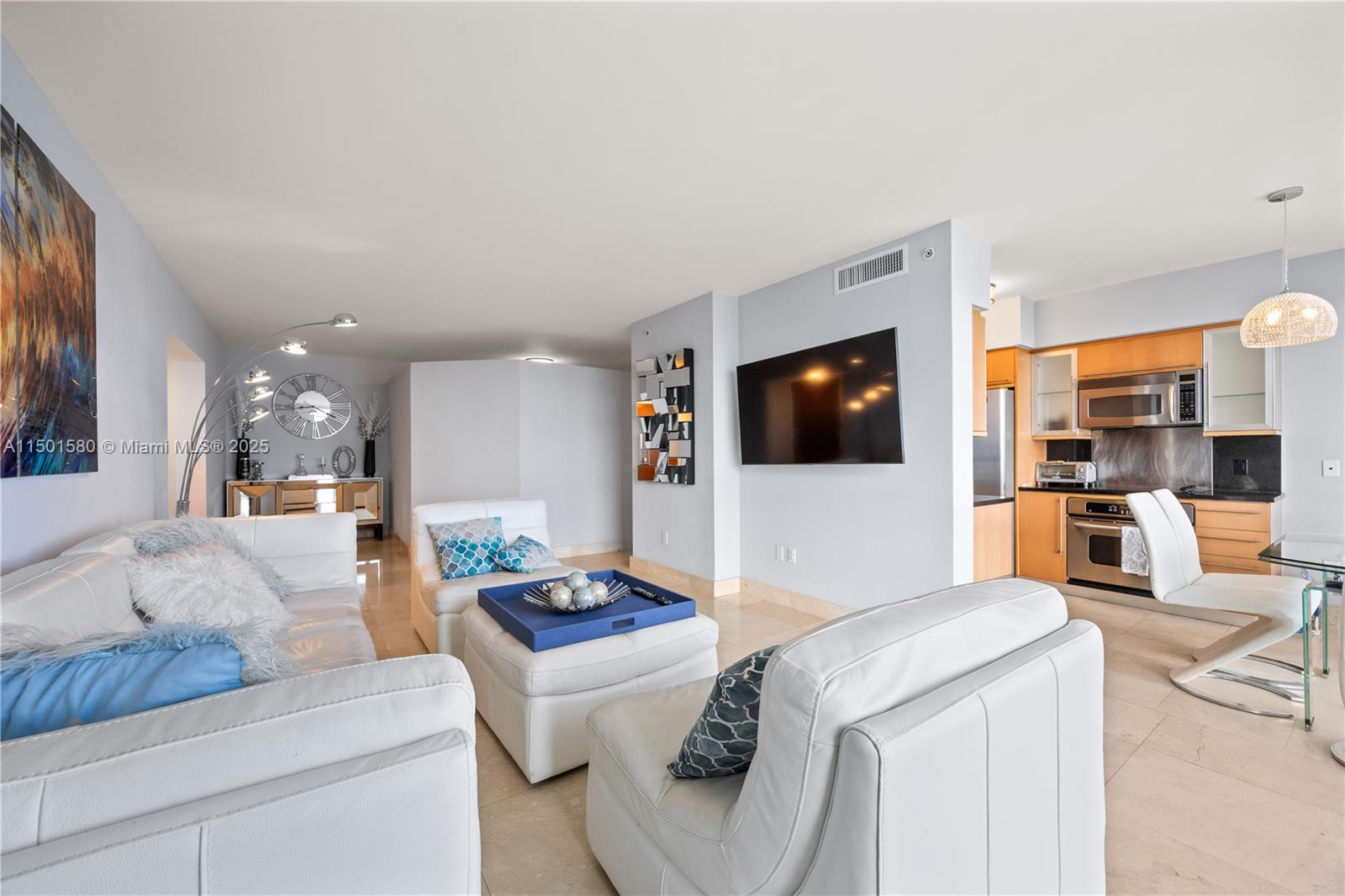 A living room with white leather furniture, a wall-mounted television, and an adjacent kitchen — 6365 Collins Ave # 4106, Miami Beach FL 33141, MIAMI BEACH, FL