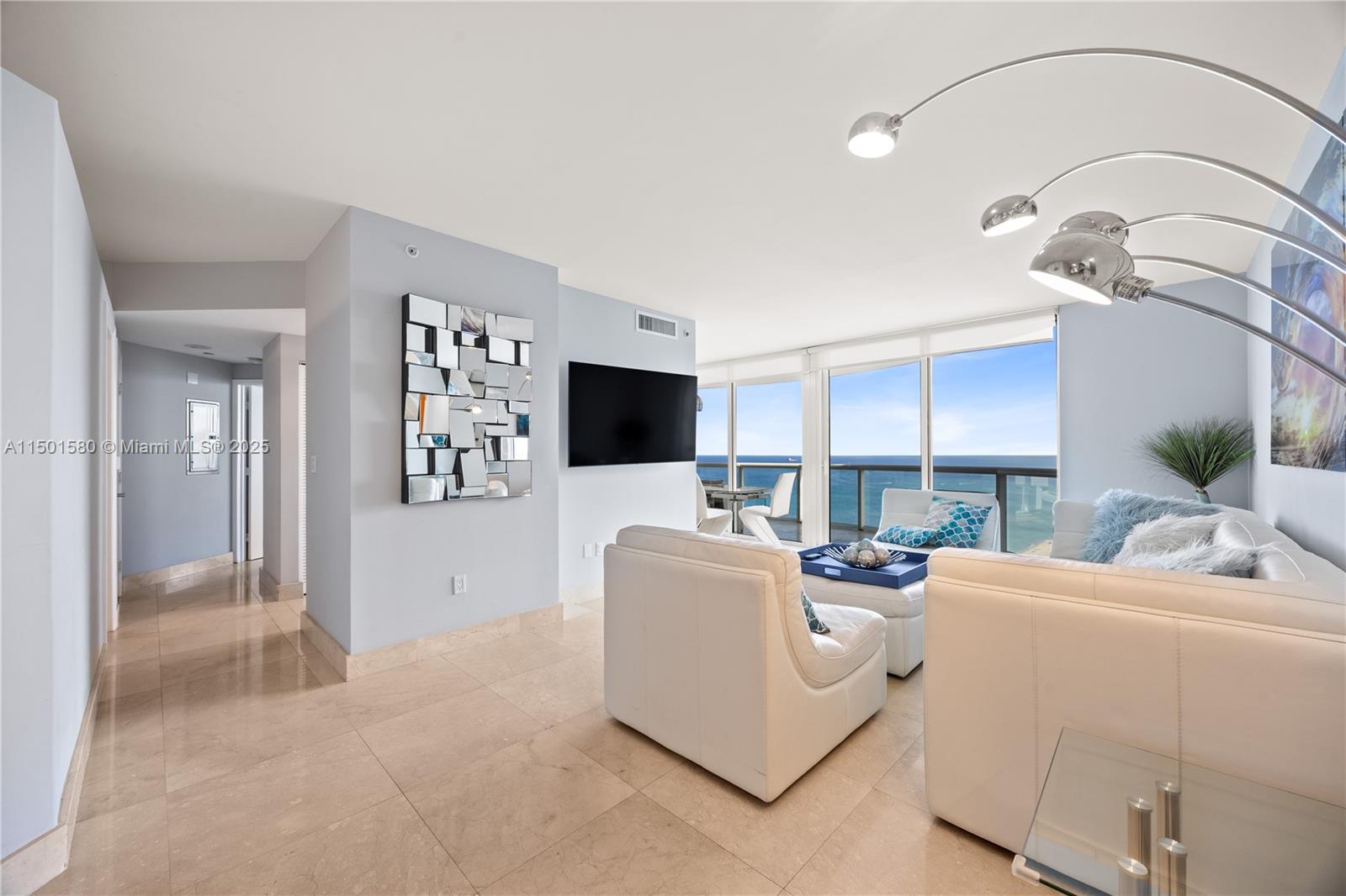 A living room with white furniture, tile floors, and floor-to-ceiling windows overlooking the ocean — 6365 Collins Ave # 4106, Miami Beach FL 33141, MIAMI BEACH, FL