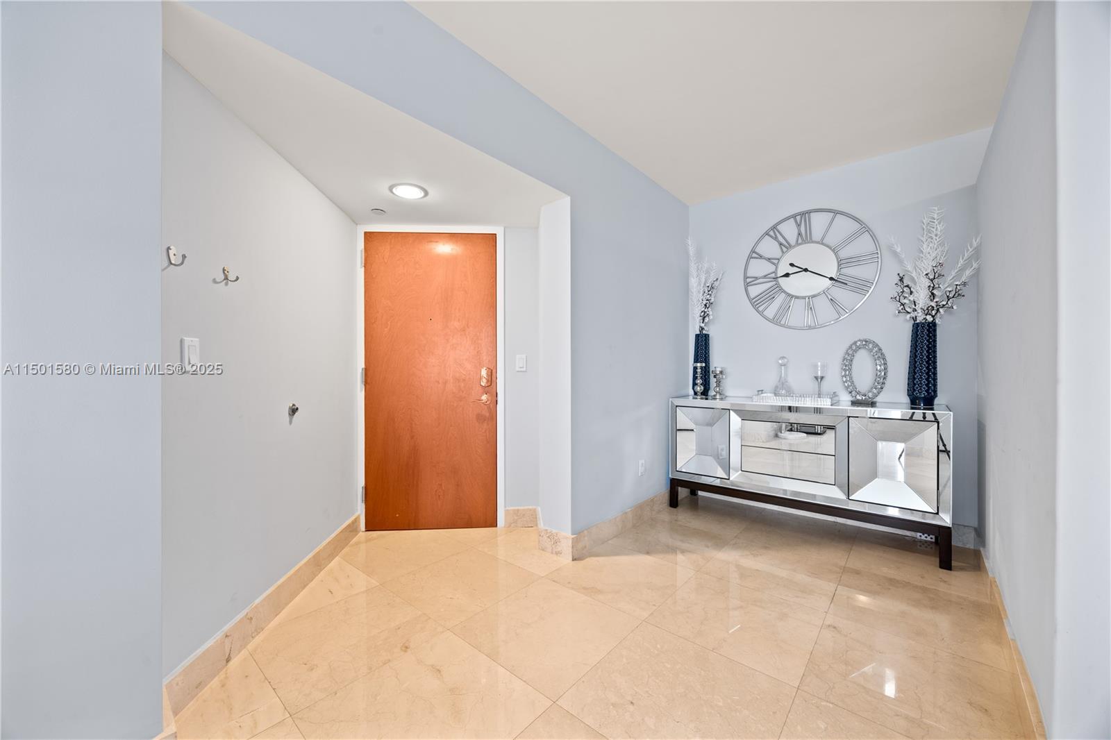 An entryway features light blue walls, beige tile flooring, a wooden door, and a mirrored console — 6365 Collins Ave # 4106, Miami Beach FL 33141, MIAMI BEACH, FL