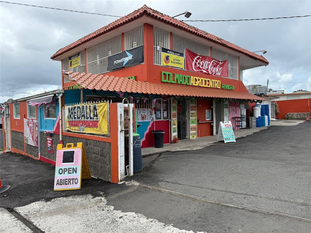 A two-story commercial building with orange walls, a tiled roof, and various advertising signs — BO CEIBA NORTE COL. AGROCENTRO RIVERA, JUNCOS, PR