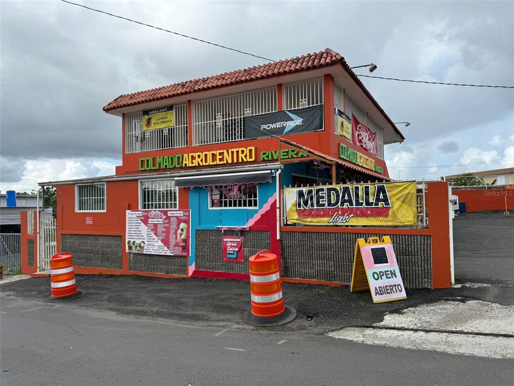 A two-story orange commercial building with a balcony, signage, and traffic barrels in front — BO CEIBA NORTE COL. AGROCENTRO RIVERA, JUNCOS, PR