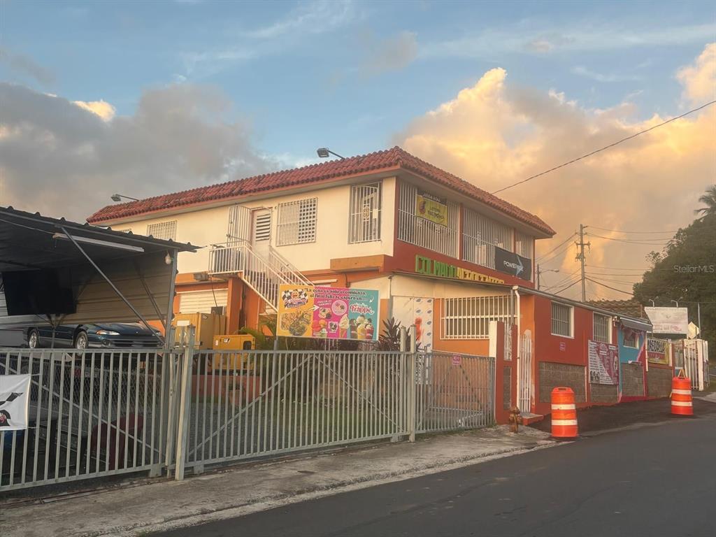 A two-story building with an orange exterior, a tiled roof, and a fenced parking area — BO CEIBA NORTE COL. AGROCENTRO RIVERA, JUNCOS, PR