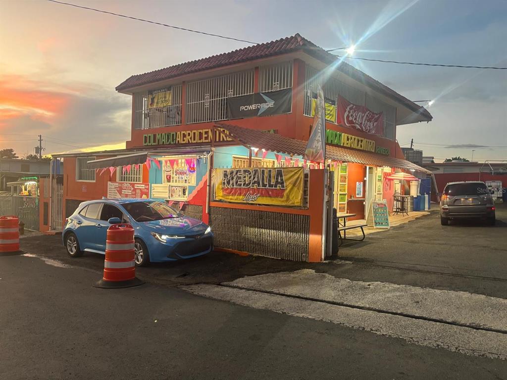 A two-story orange commercial building with a Medalla Light banner and parked cars outside — BO CEIBA NORTE COL. AGROCENTRO RIVERA, JUNCOS, PR