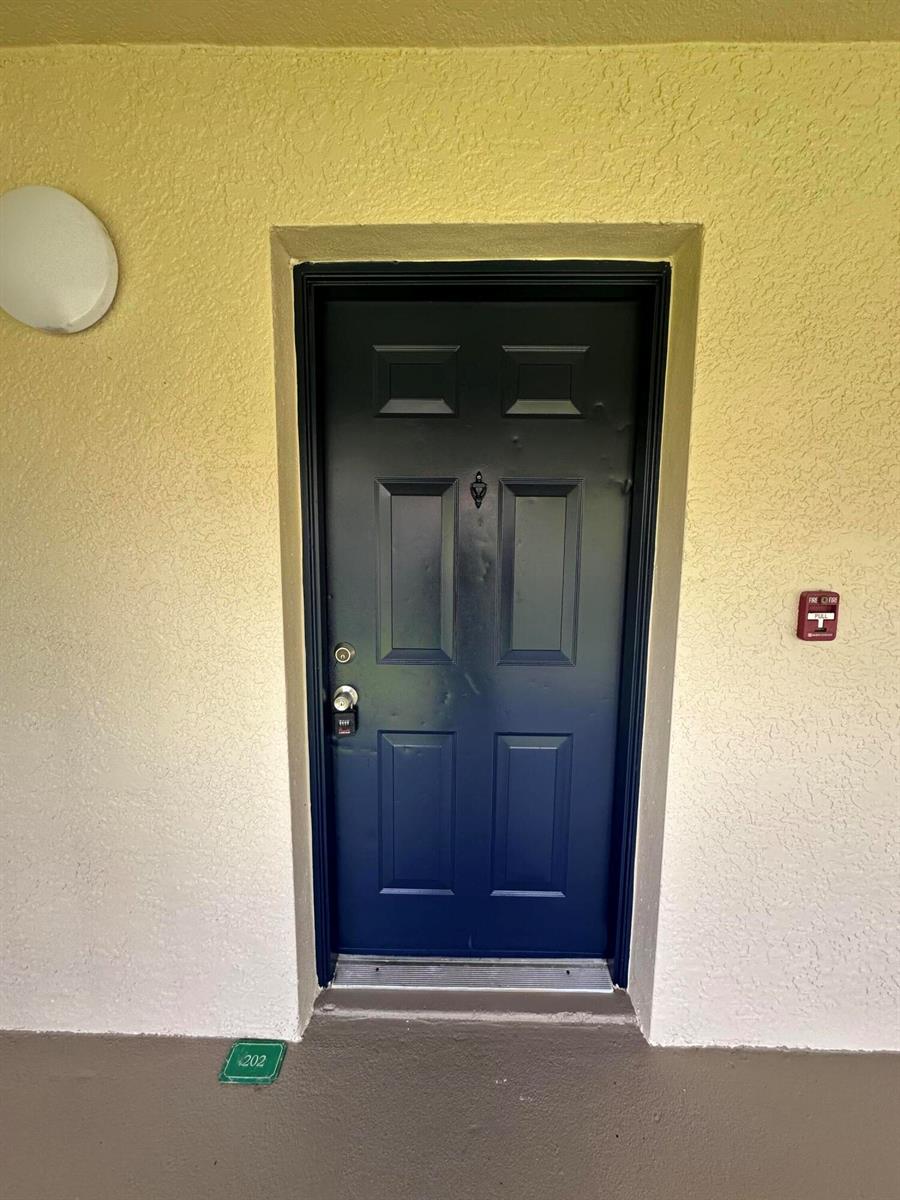 A dark blue front door with a silver knob is set into a yellow wall — 141 SW Palm Drive # 202, FL 34986, FL