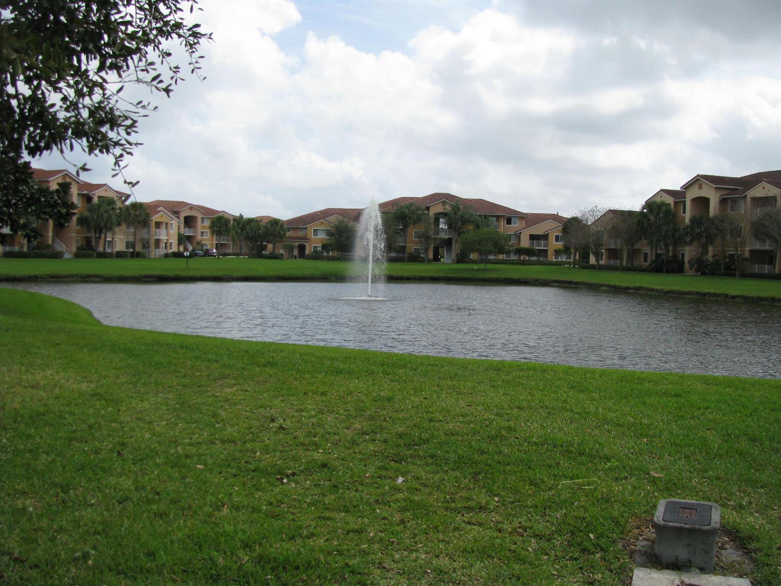 A pond with a central fountain sits in front of multi-story apartment buildings and grass — 141 SW Palm Drive # 202, FL 34986, FL