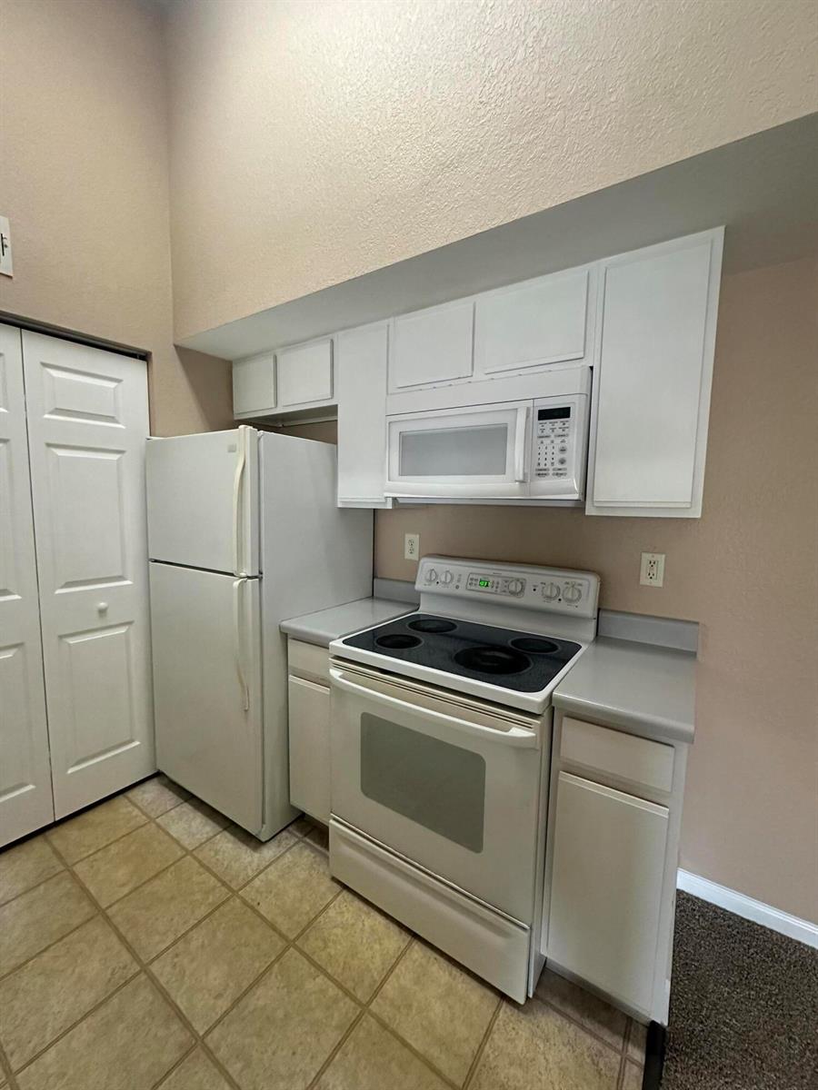 A kitchen features white cabinets, a white refrigerator, and a white electric range — 141 SW Palm Drive # 202, FL 34986, FL