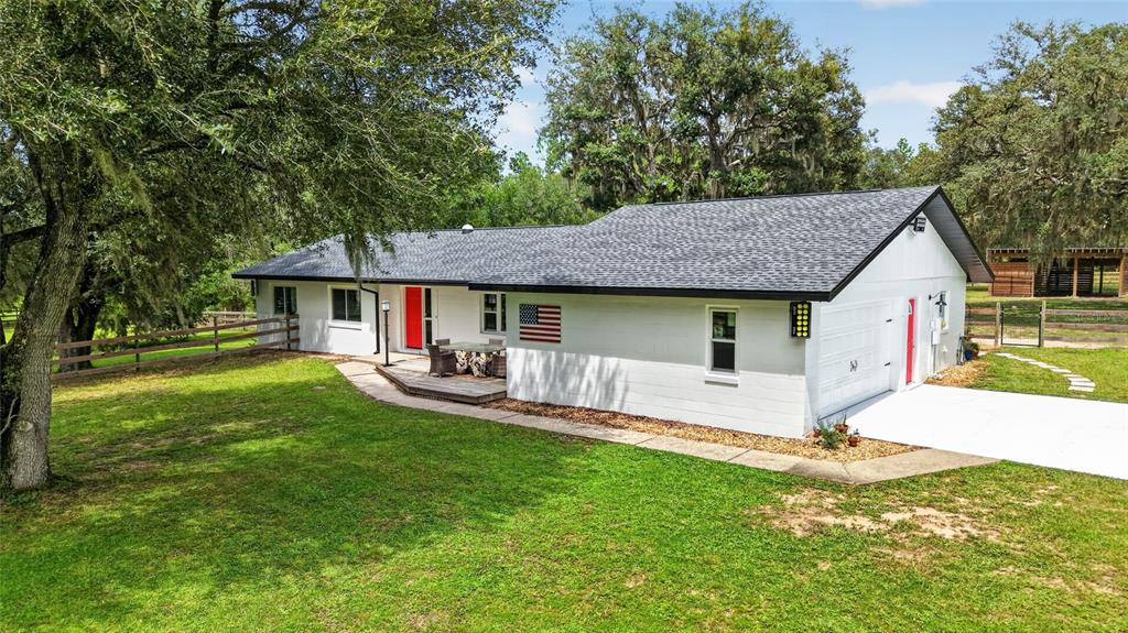 A white, single-story house with a dark shingled roof, an American flag, and a garage — 11281 N CIRCLE M AVENUE, DUNNELLON, FL