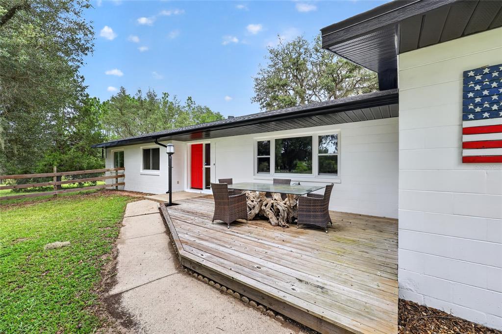 A white house exterior features a wooden deck with a glass-topped table and wicker chairs — 11281 N CIRCLE M AVENUE, DUNNELLON, FL