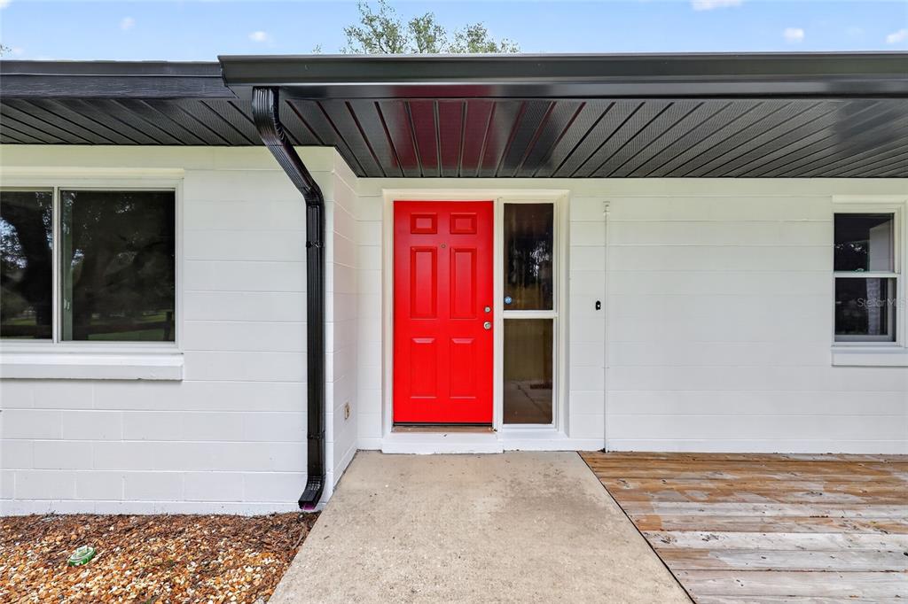 A bright red front door is centered on the white exterior wall of a house — 11281 N CIRCLE M AVENUE, DUNNELLON, FL