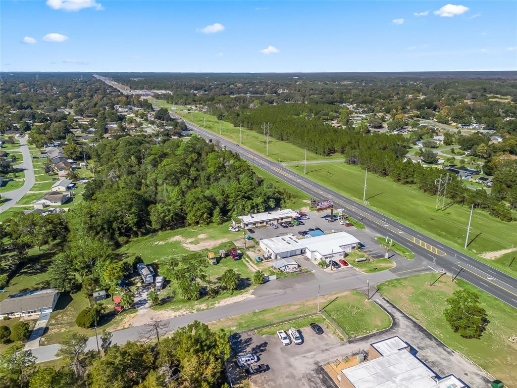 An aerial view shows commercial buildings, a parking lot, and a highway surrounded by trees — 9594 SE MARICAMP ROAD, OCALA, FL