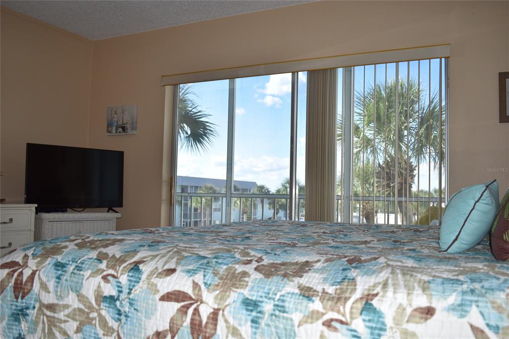 A bedroom features a floral bedspread, a television on a stand, and sliding glass balcony doors — 325 N CAUSEWAY UNIT C 304, NEW SMYRNA BEACH, FL