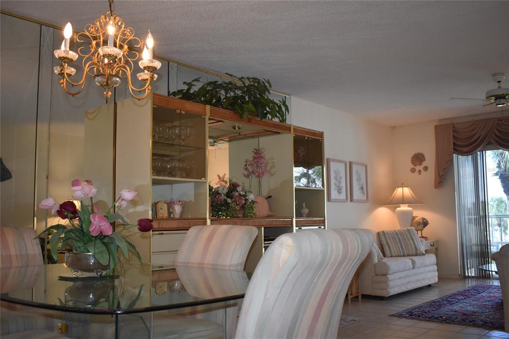 A dining area with a glass table and chandelier opens into a living room with furniture — 325 N CAUSEWAY UNIT C 304, NEW SMYRNA BEACH, FL