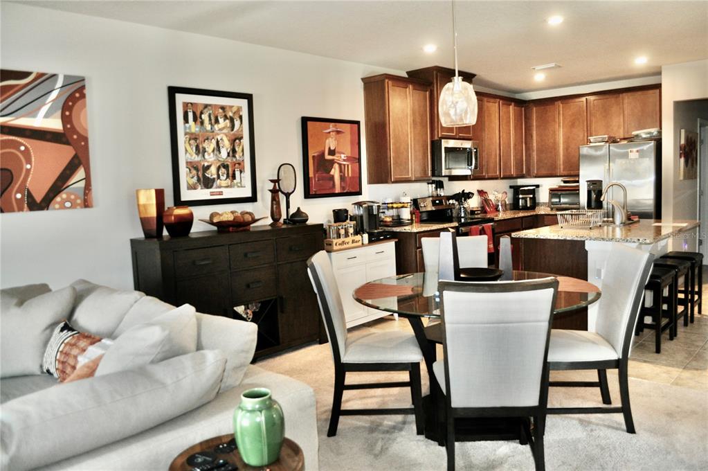 An open-concept kitchen and dining area features dark wood cabinetry, stainless appliances, and a glass-topped table — 17945 TURNING LEAF CIRCLE, LAND O LAKES, FL