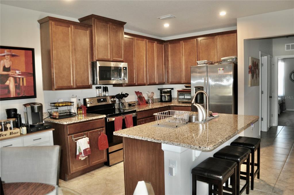 A kitchen features wood cabinets, granite countertops, stainless steel appliances, and a central island — 17945 TURNING LEAF CIRCLE, LAND O LAKES, FL
