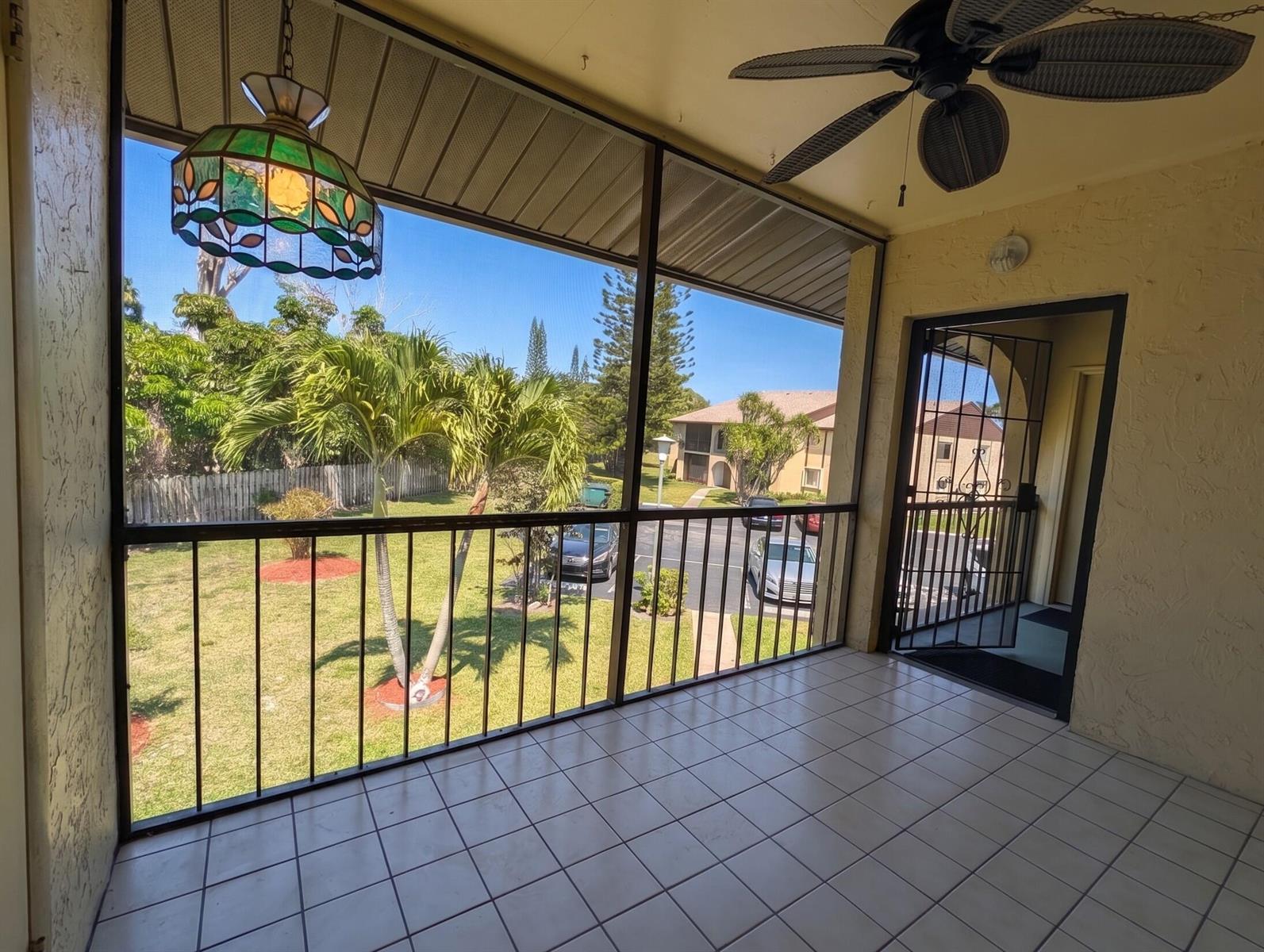 A screened-in balcony with white tile flooring, a ceiling fan, and a view of palm trees — 327 Pine Ridge Circle # 2, FL 33463, FL