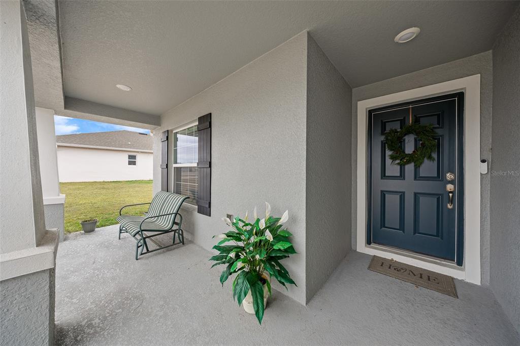 A covered front porch features a dark blue door, a striped chair, and a potted plant — 8992 SE 42ND COURT, OCALA, FL