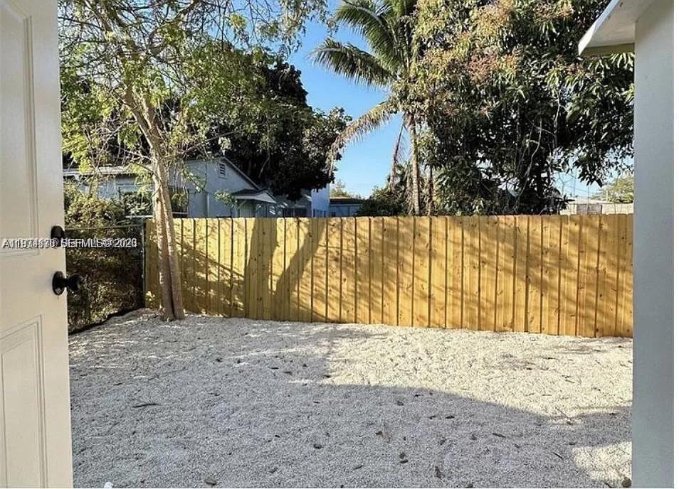 A fenced backyard features a gravel ground surface and several trees under a clear sky — 101 NW 68th Ter, Miami FL 33150, MIAMI, FL