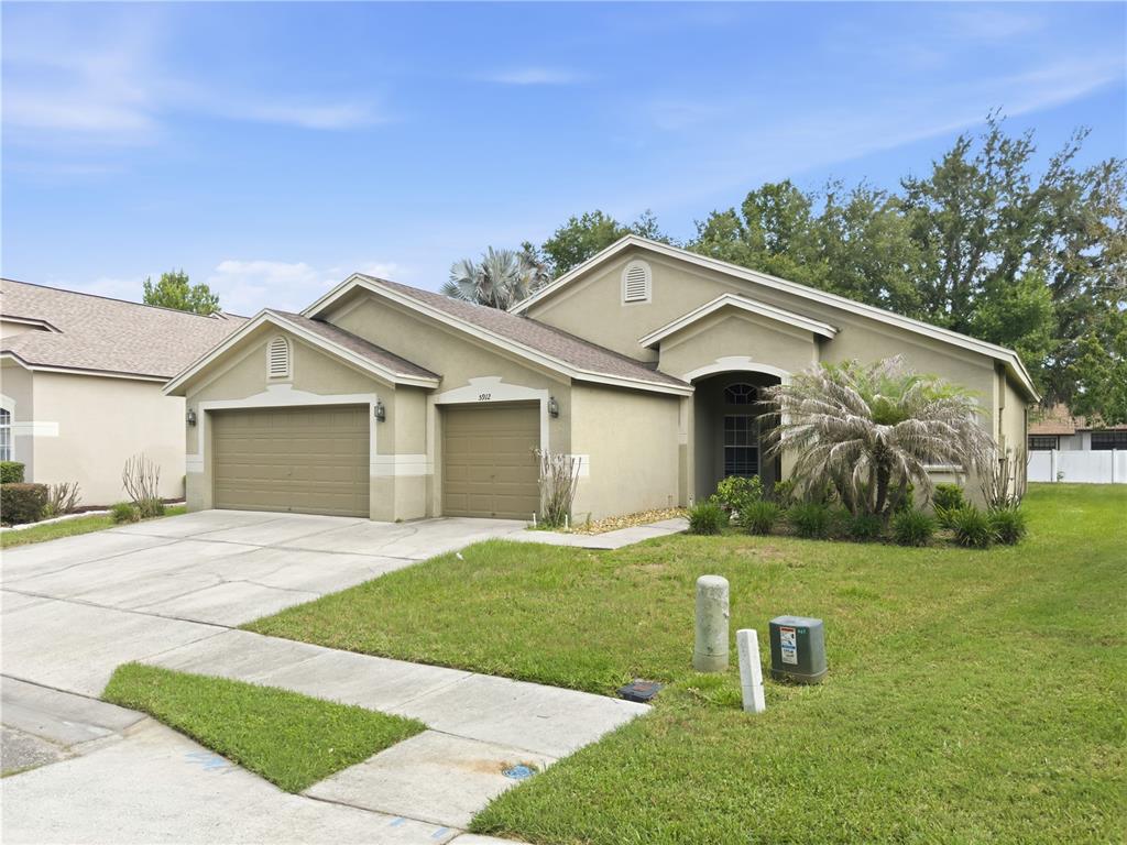 A single-story suburban house with a three-car garage and a beige stucco exterior — 5912 BRAMBLE BUSH COURT, ZEPHYRHILLS, FL