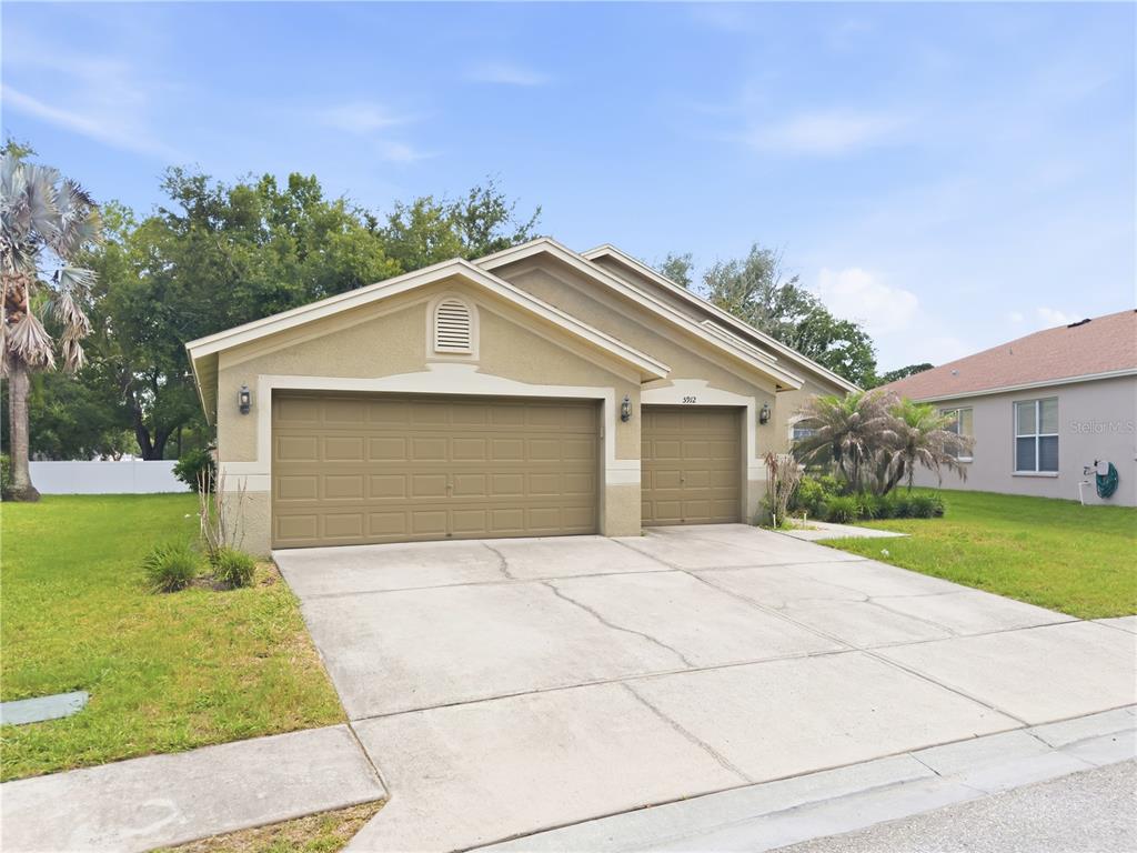 A tan, single-story house with a three-car garage and a concrete driveway — 5912 BRAMBLE BUSH COURT, ZEPHYRHILLS, FL