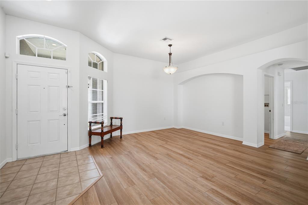 A bright entryway and dining area feature white walls, wood-look flooring, and a tiled foyer — 5912 BRAMBLE BUSH COURT, ZEPHYRHILLS, FL