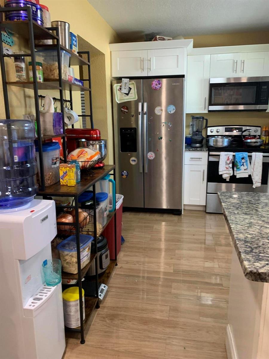 A kitchen features stainless steel appliances, white cabinetry, granite countertops, and a metal shelving unit — 1014 Old Boynton Road, Boynton Beach FL 33426, BOYNTON BEACH, FL