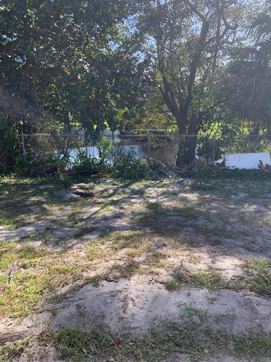 A grassy backyard features sandy patches, mature trees, and a chain-link fence bordering a canal — 1014 Old Boynton Road, Boynton Beach FL 33426, BOYNTON BEACH, FL