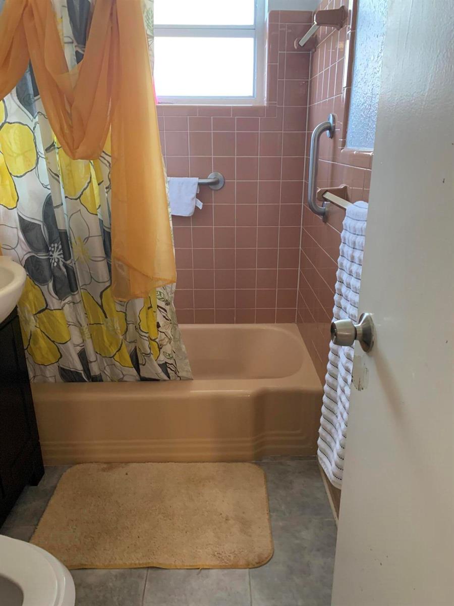 A bathroom features a peach-colored bathtub, pink wall tiles, and a yellow floral shower curtain — 1014 Old Boynton Road, Boynton Beach FL 33426, BOYNTON BEACH, FL