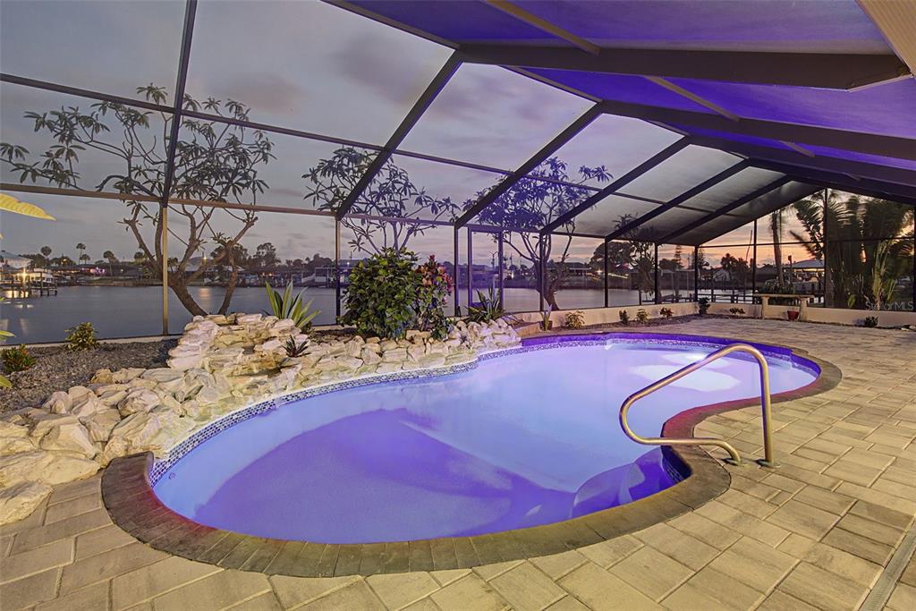 A screened-in pool area features a rock waterfall, stone pavers, and a view of water — 728 SPANISH MAIN DRIVE, APOLLO BEACH, FL
