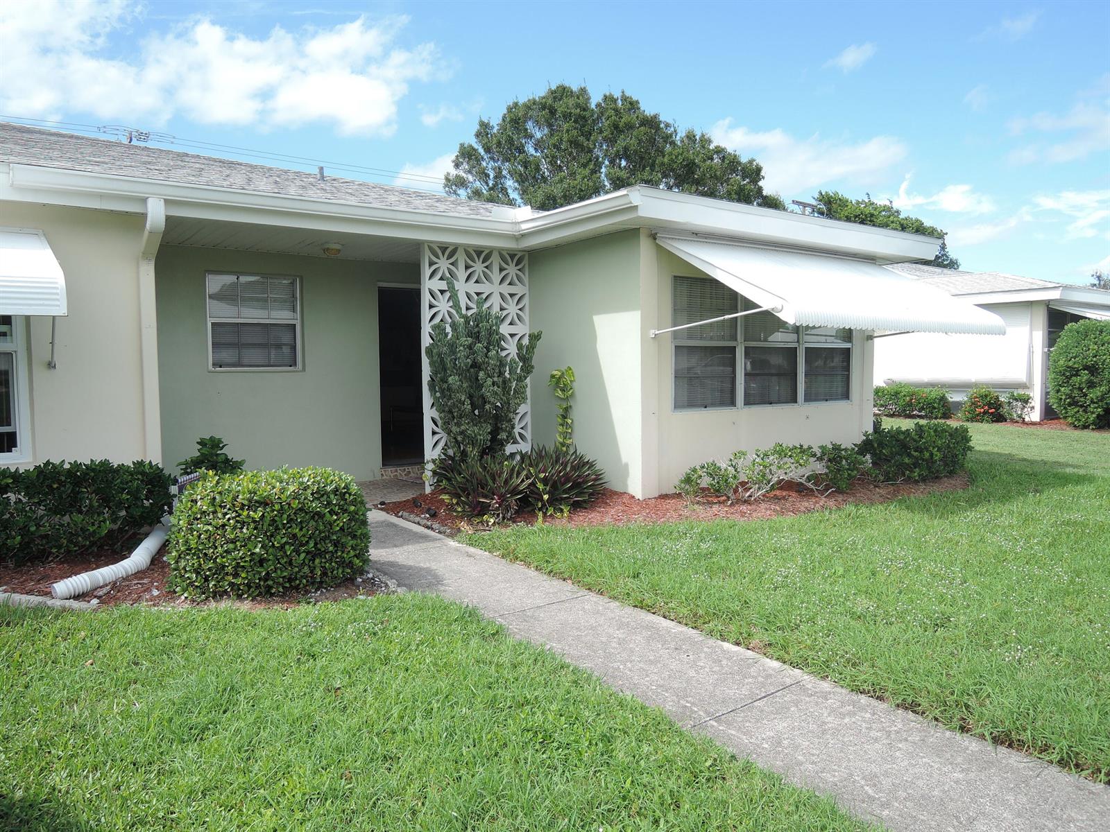 A light green single-story house features a decorative breeze block screen and white awnings — 115 Lakes End Drive Apt D, Fort Pierce FL 34982, FORT PIERCE, FL