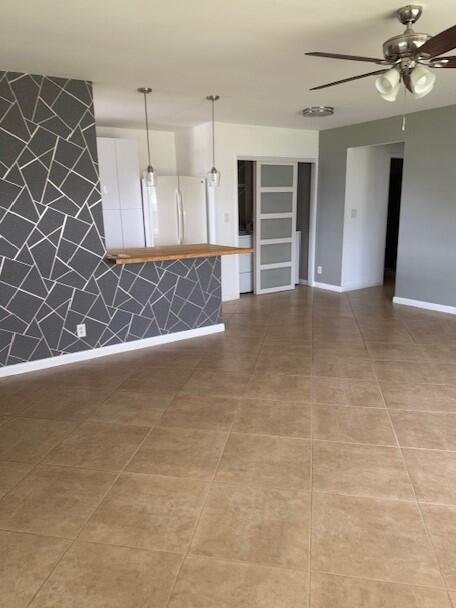 A living room with tan tile floors, a geometric accent wall, and a kitchen breakfast bar — 115 Lakes End Drive Apt D, Fort Pierce FL 34982, FORT PIERCE, FL