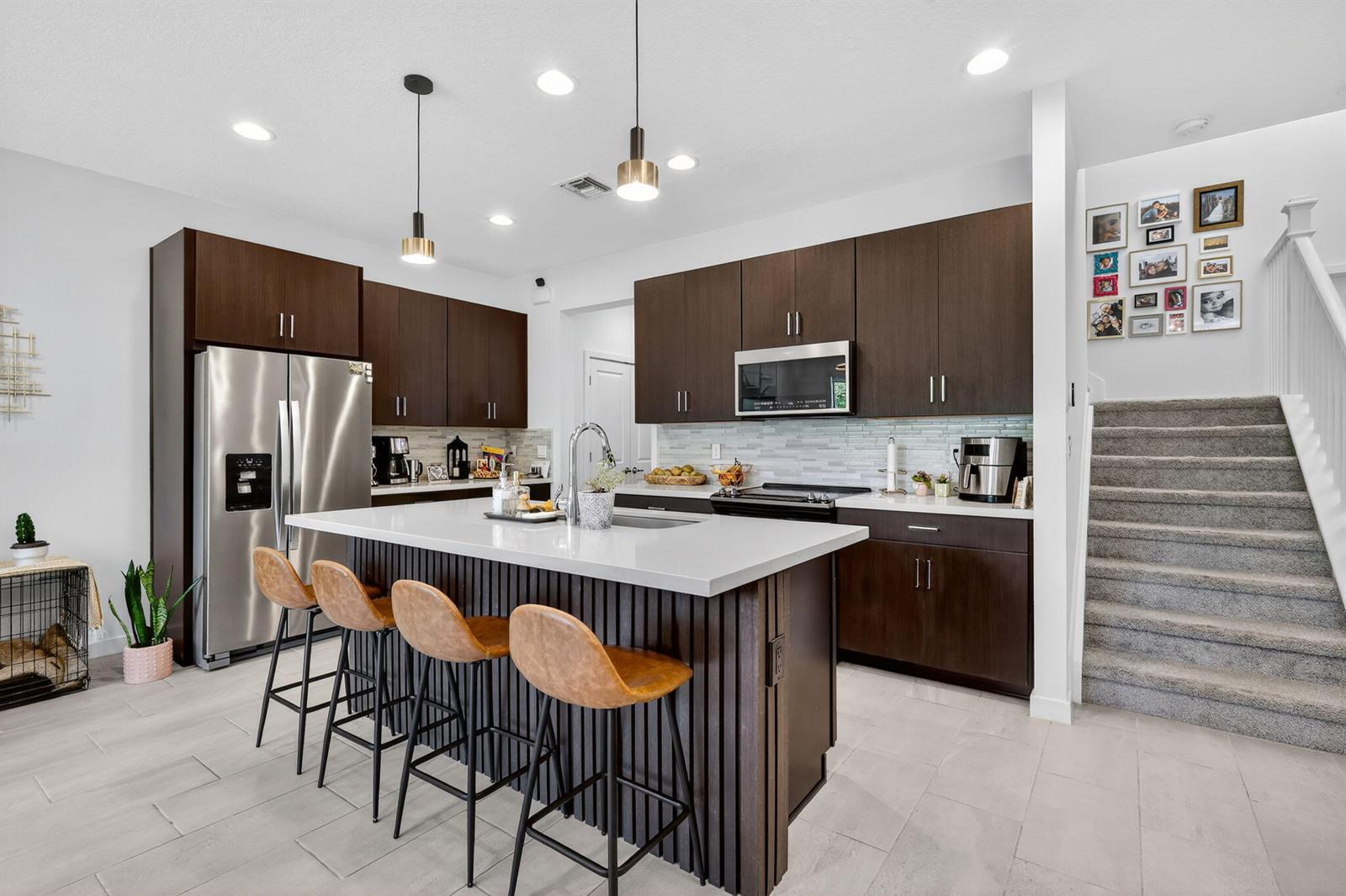 A modern kitchen features dark wood cabinetry, a white quartz island, and a carpeted staircase — 4388 Serpens Lane, Lake Worth FL 33467, LAKE WORTH, FL