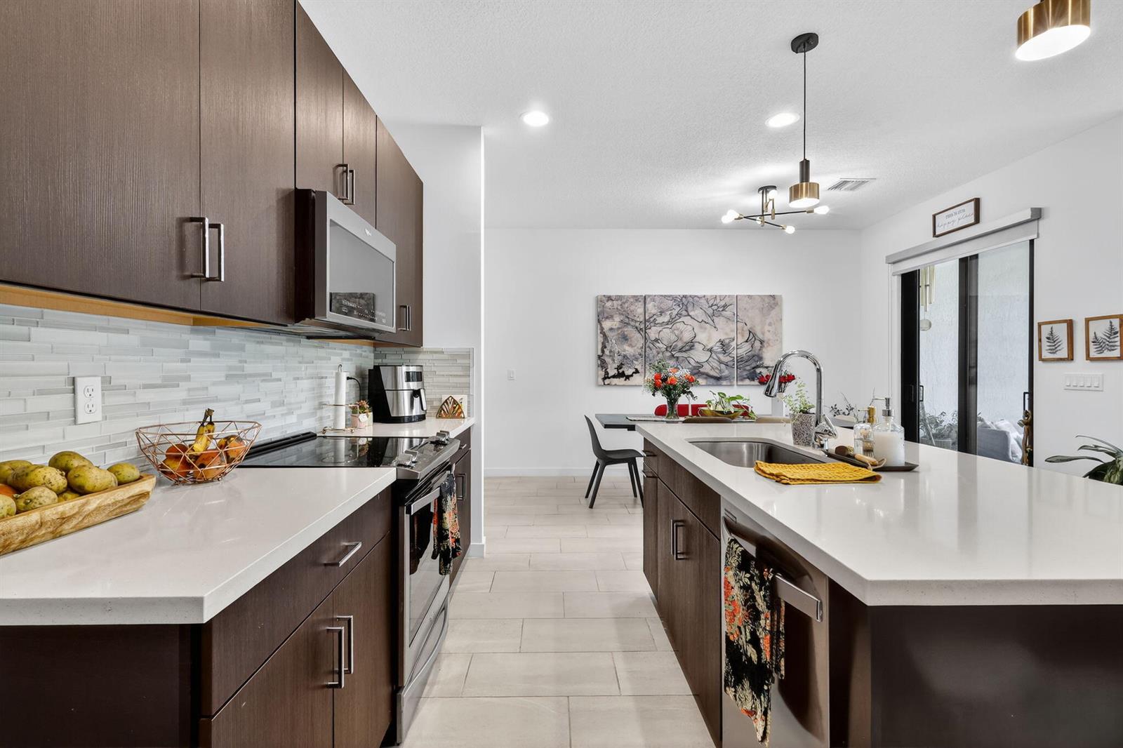 A modern kitchen features dark wood cabinets, white countertops, stainless steel appliances, and an island — 4388 Serpens Lane, Lake Worth FL 33467, LAKE WORTH, FL