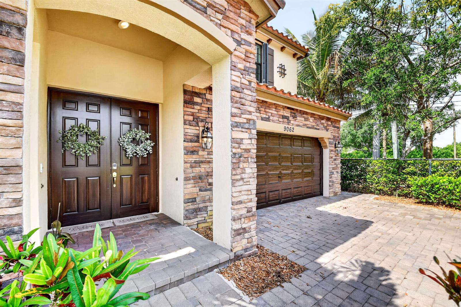 A stone-accented house exterior features a double front door, a garage, and a paved driveway — 9062 Gulf Cove Drive, Wellington FL 33467, WELLINGTON, FL