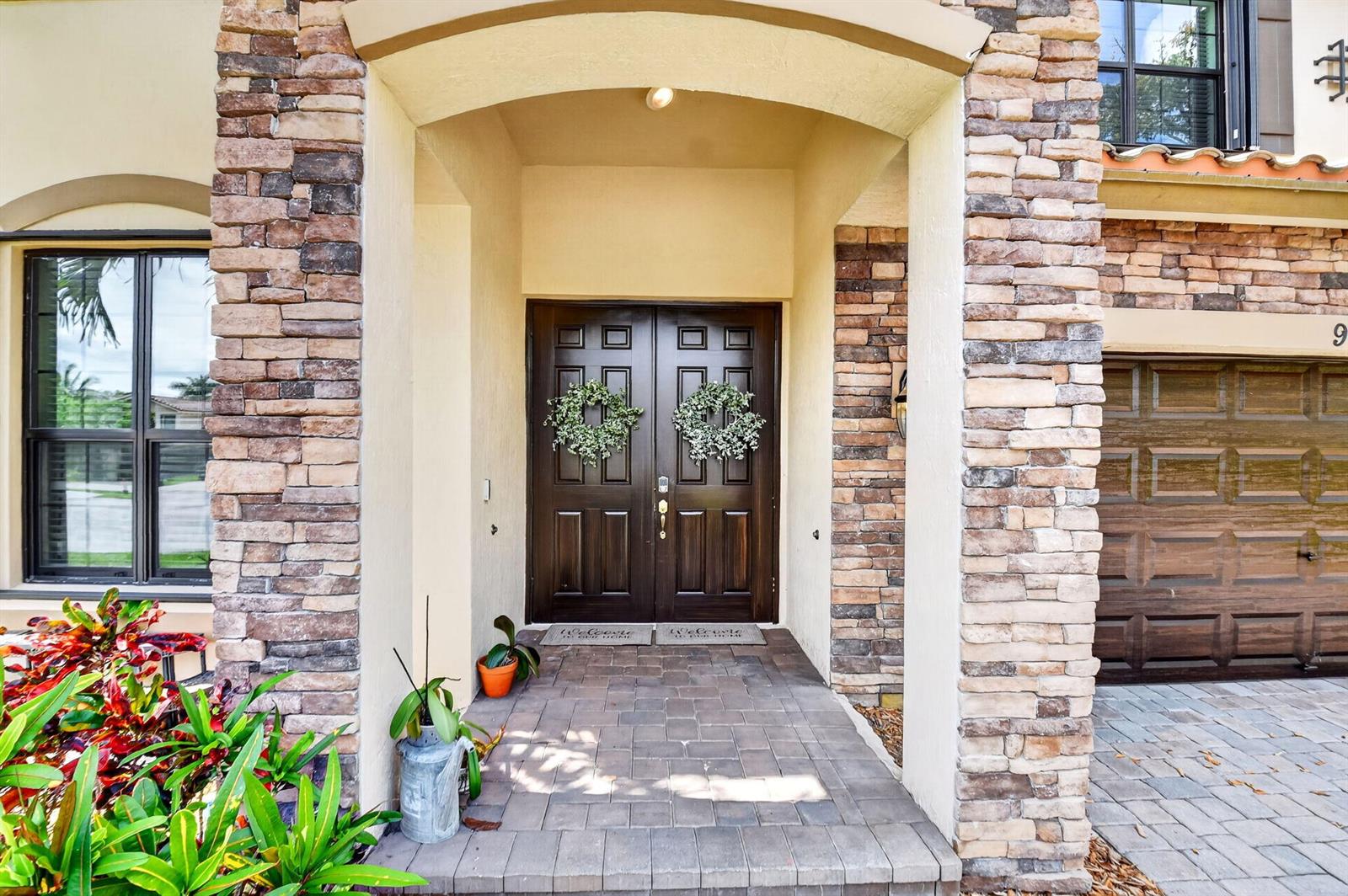 A stone-accented entryway features a double front door with wreaths and a paved porch — 9062 Gulf Cove Drive, Wellington FL 33467, WELLINGTON, FL